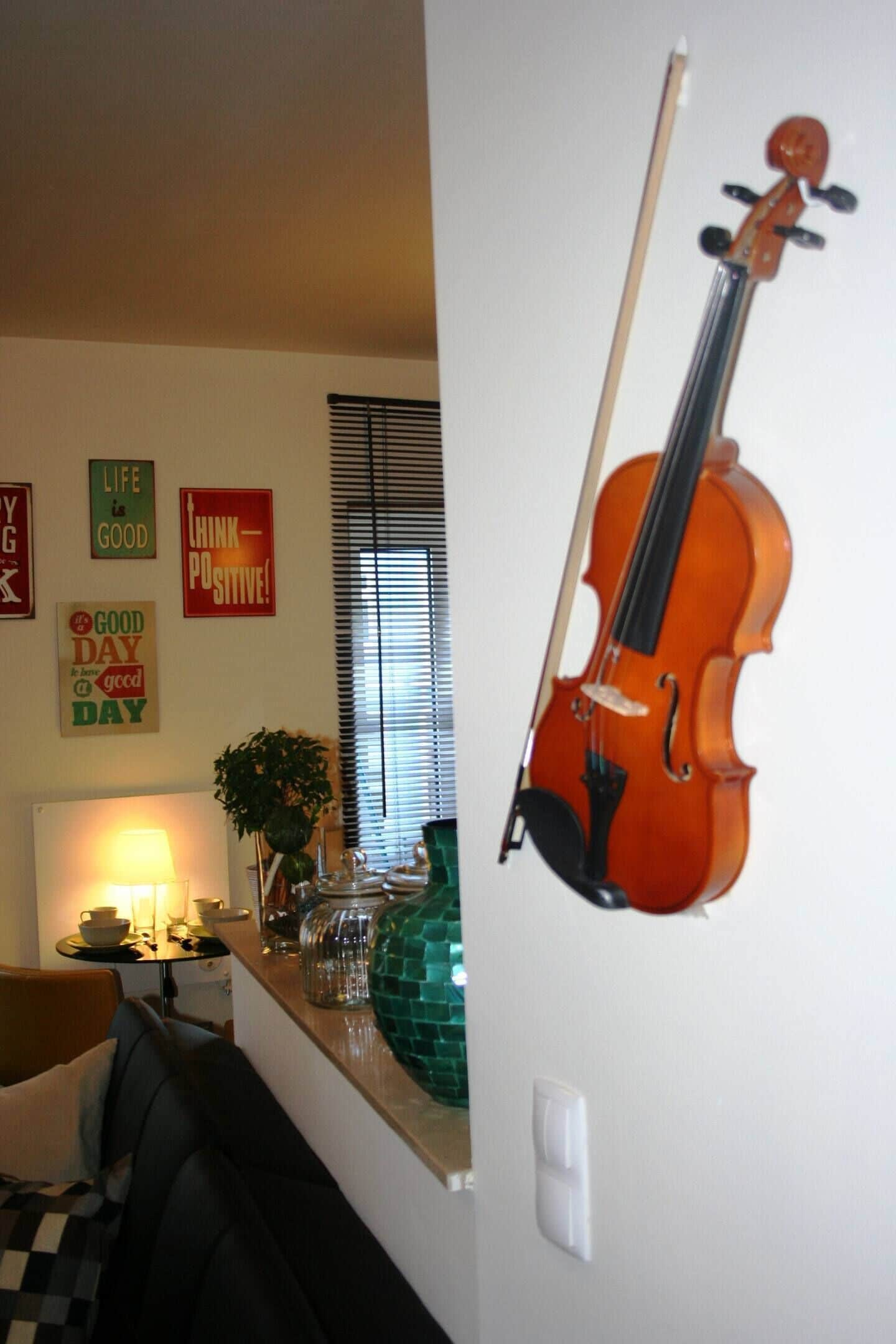 Ett vardagsrum med en fiol lutad mot väggen, en soffa, ett bord med en lampa och motivationsaffischer.