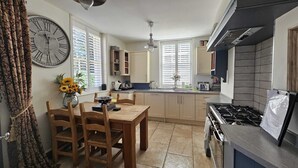 Una cocina con armarios de madera, una mesa de comedor con sillas, un reloj grande y una estufa a gas.