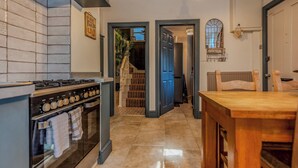 Una cocina con estufa, horno y salpicadero de azulejos. Hay una mesa de madera y sillas en la zona de comedor.