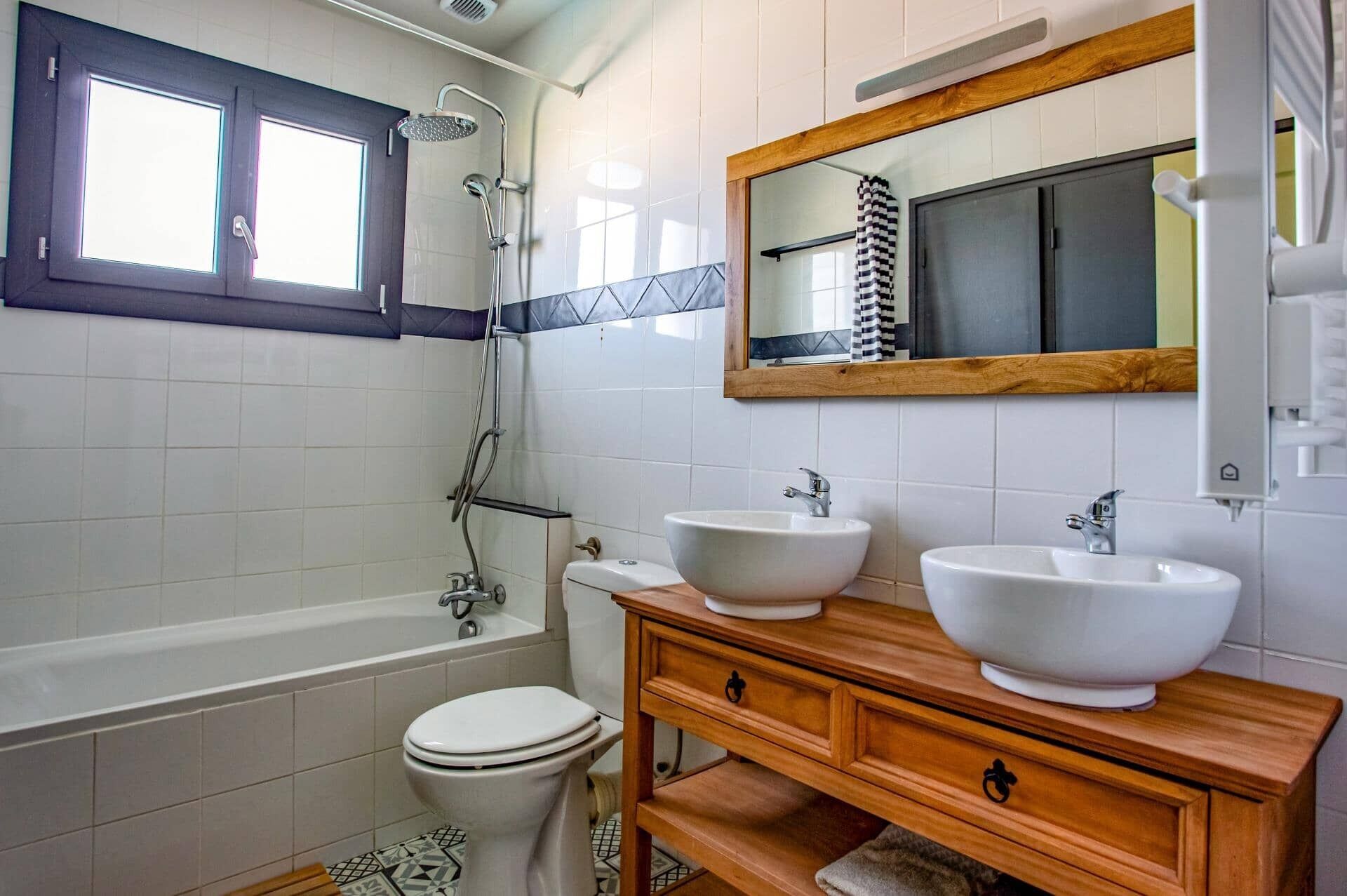 A bathroom with a bathtub, two sinks, a toilet, and a window.