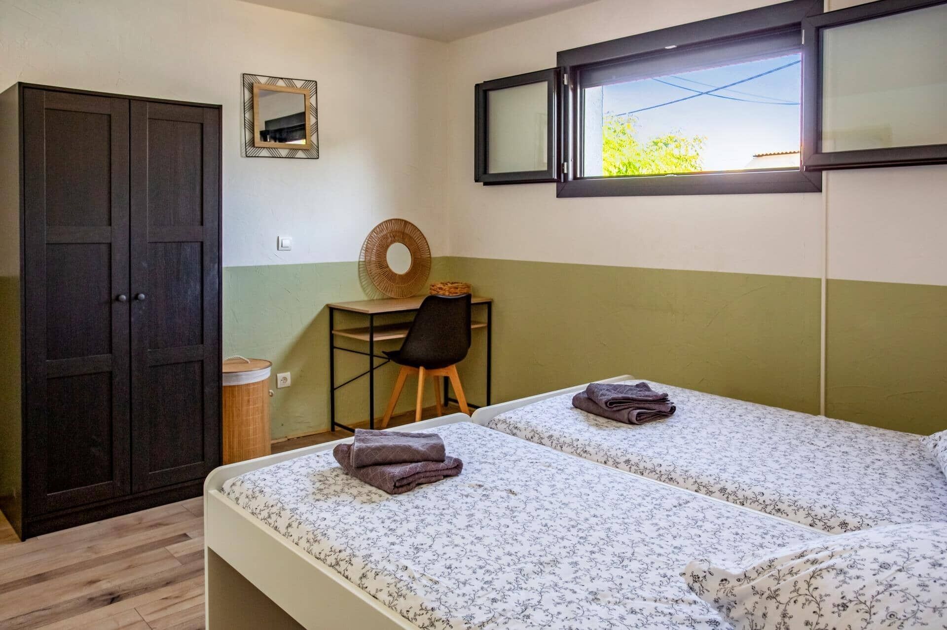 Ein Zimmer mit zwei Betten, einem Schreibtisch, einem Stuhl, einem Kleiderschrank und einem Fenster mit Blick.
