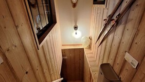 Una escalera de madera conduce a una habitación pequeña con un accesorio de iluminación, un espejo y un soporte para esquíes.
