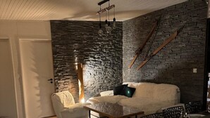 Una sala de estar acogedora con una pared de piedra, un sofá blanco, una mesa de centro de madera y una chimenea.