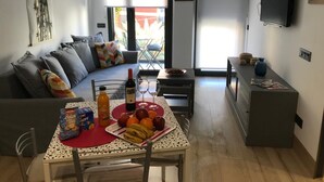 Un soggiorno moderno con divano, tavolo da pranzo con cibo e bevande, televisione e balcone con vista.