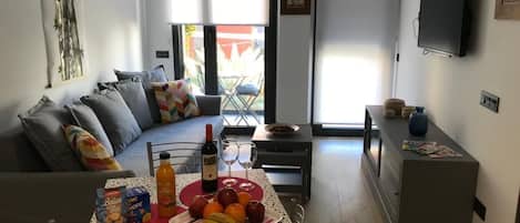 Una sala de estar moderna con un sofá, una mesa de comedor con comida y bebidas, un televisor y un balcón con vistas.