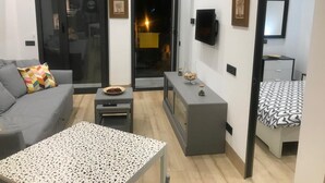 Un soggiorno moderno con un divano grigio, un tavolino da caffè decorato, una TV a parete e un letto con copripiumino a motivi geometrici.