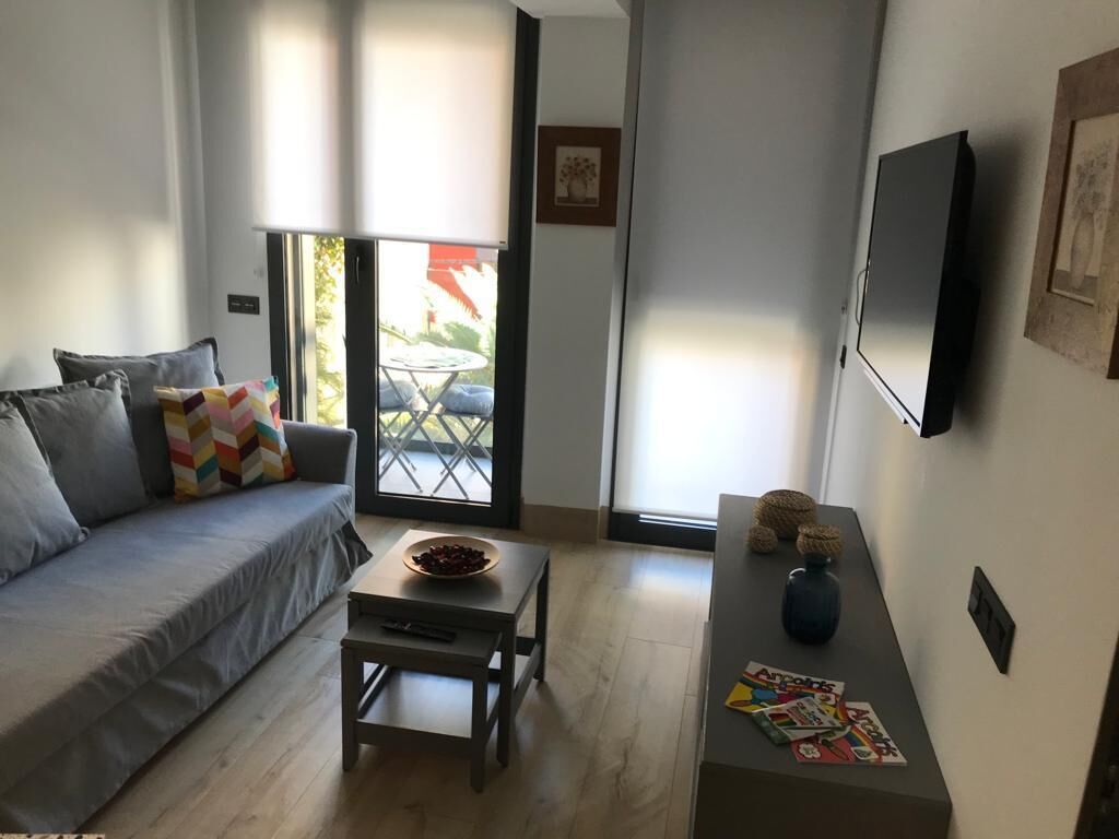 Un salón con sofá, una mesa de centro, televisor y un ventanal corredizo que da a un espacio al aire libre.