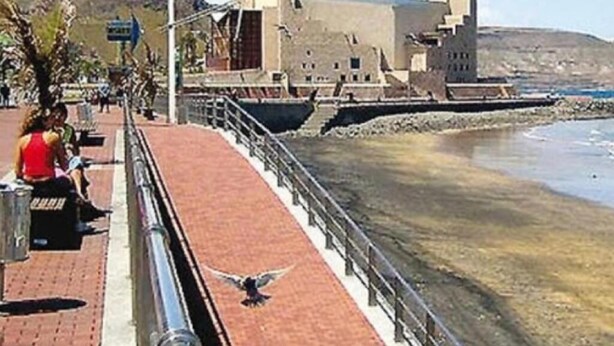 Una passeggiata costiera con un uccello sul sentiero, un edificio con una cupola sullo sfondo e un cielo sereno.