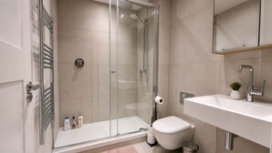 Un baño moderno con cabina de ducha de vidrio, inodoro blanco, lavabo con espejo y una pequeña planta en maceta.