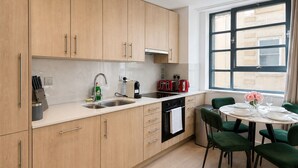 Una cocina moderna con armarios de madera, un lavamanos, un tostador y una zona de comedor con sillas verdes y una mesa.