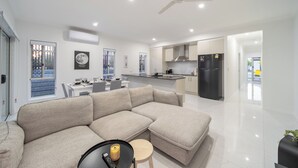 Uma sala de estar moderna com sofá seccional, área de jantar e cozinha com geladeira preta.