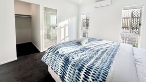Quarto com cama, ventilador de teto, janela e porta que dá para uma varanda.