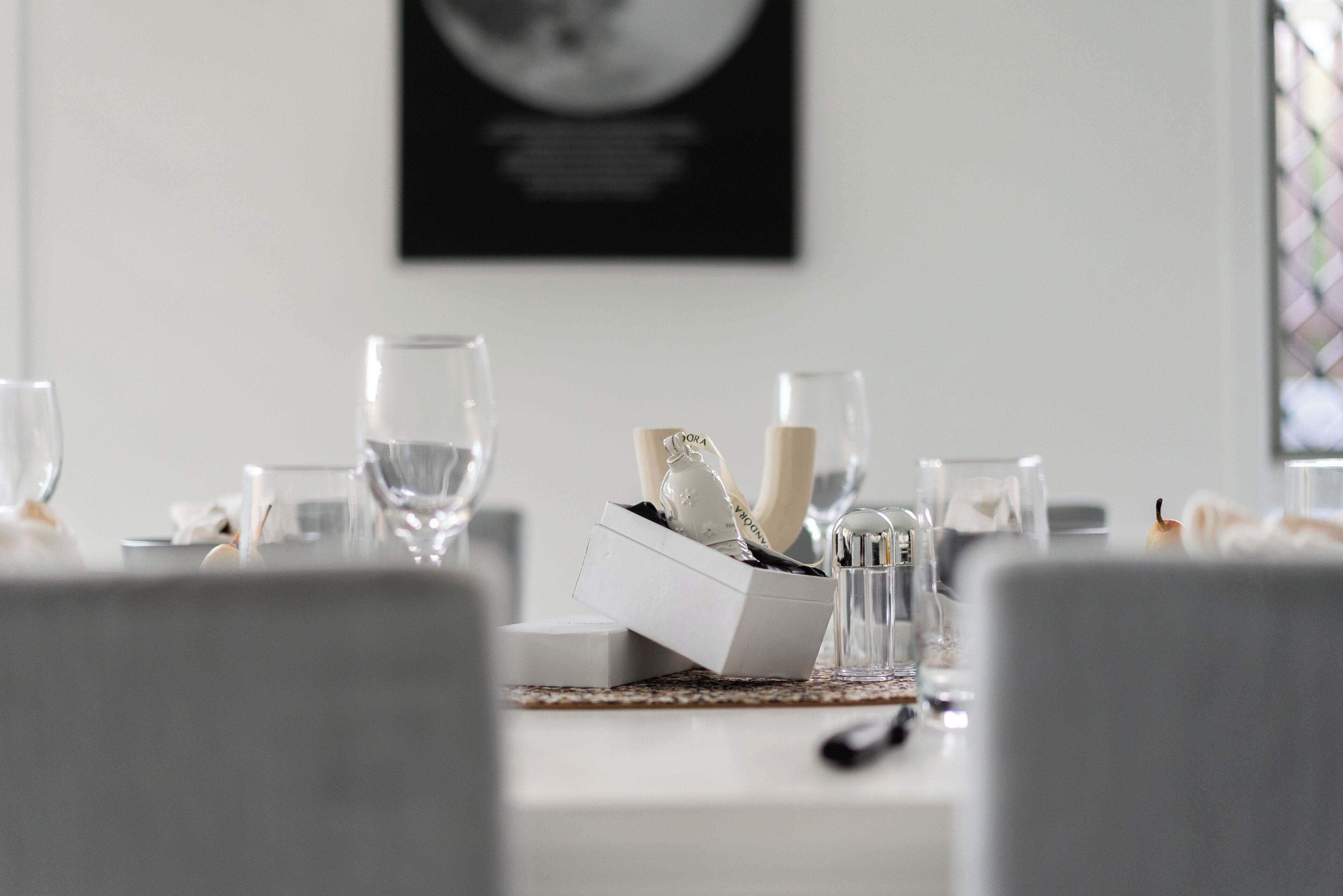 Una mesa de comedor dispuesta con vasos transparentes, una vela y una caja de cubiertos.