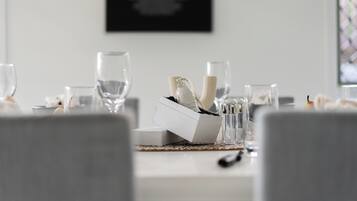 Una mesa de comedor dispuesta con vasos transparentes, una vela y una caja de cubiertos.
