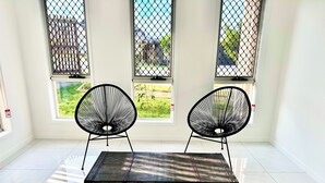 Quarto com um banco, duas cadeiras e grandes janelas com vista para um jardim.