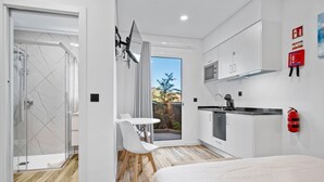 Una habitación de hotel moderna con cama, una kitchenette pequeña, un baño con ducha de vidrio y un comedor con vistas.