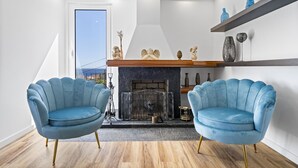 A modern living room with a fireplace, two blue armchairs, and a wooden floor. - São Lourenço Guest House (Machico)
