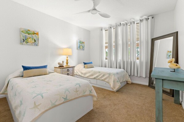 A bedroom with two beds, a ceiling fan, a nightstand with a lamp, and a mirror.