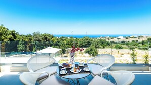 Ein Balkon mit Tisch für zwei Personen, der auf eine reizvolle Landschaft mit Bäumen und Meerblick blickt.