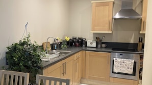 A compact kitchen with wooden cabinets, a stainless steel range hood, a coffee maker, a toaster, and a dishwashing unit.