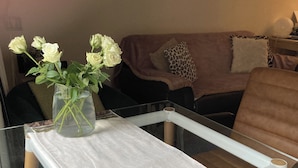 A glass table with a white cloth, a vase with white flowers, and a blue rug.
