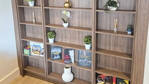 Een houten boekenkast met meerdere planken, waarvan sommige boeken en decoratieve objecten bevatten, en andere kleine potplanten.