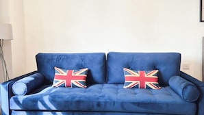Een blauwe bank met twee kussens met het Union Jack-design, staand in een kamer met een houten vloer en een witte muur.