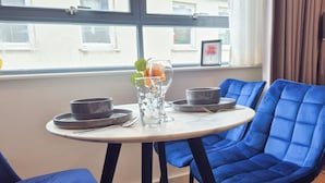 Een eetgedeelte met een ronde tafel, blauwe bekleden stoelen en een raam met uitzicht op gebouwen.