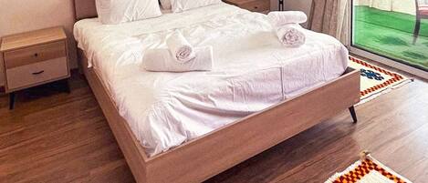 A hotel room with a bed, bedside tables, a coat rack, and a view of the outdoors.