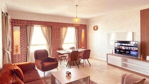 A living room with a brick accent wall, a television, and a dining area with chairs and a table. - ZAYANE HOMES AGADIR (Agadir)