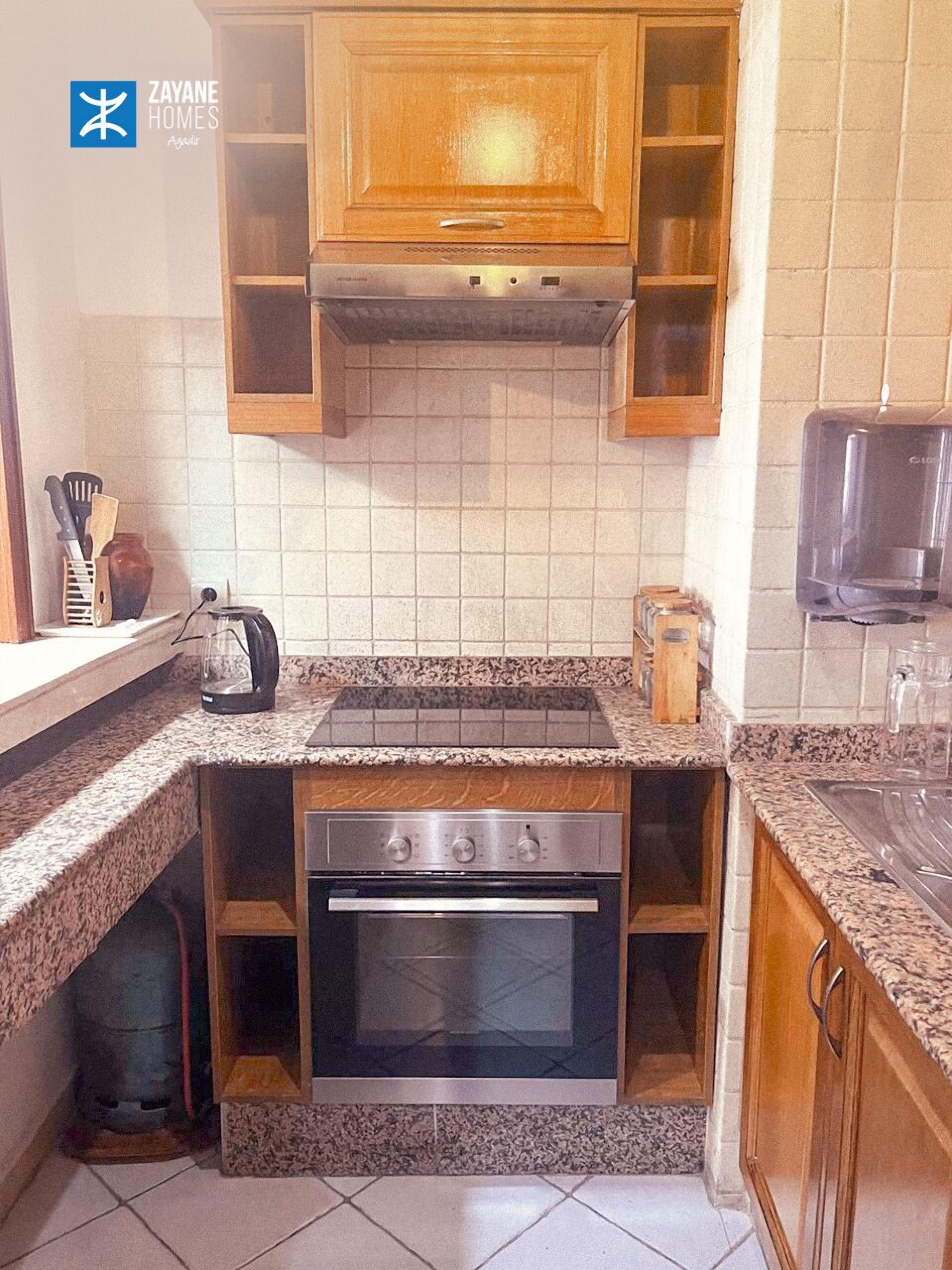 A compact kitchen with a built-in oven, a stovetop, wooden cabinets, and a tiled backsplash.