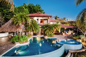 A resort with a swimming pool, outdoor seating, and a thatched-roof structure.