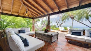 A covered outdoor seating area with a wooden ceiling, white cushioned sofas, and a central table with a flower arrangement. - Enchanting 6 Bedroom Villa with Incredible Views- Fully Staffed -Walk to Beach (Tamarindo)