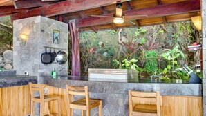 A stone bar with wooden chairs, a ceiling fan, and a view of the surrounding garden. - Enchanting 6 Bedroom Villa with Incredible Views- Fully Staffed -Walk to Beach (Tamarindo)