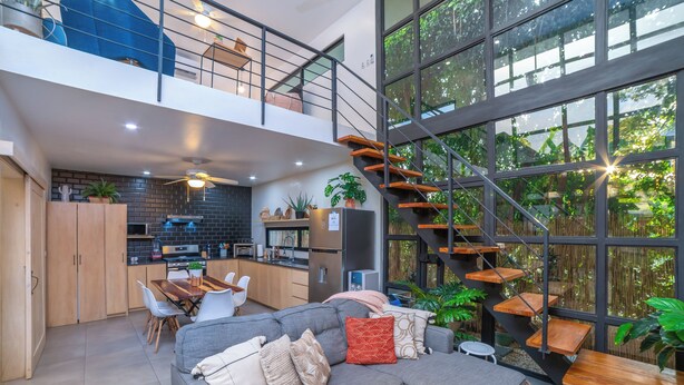Ein modernes Interieur mit Essbereich, einem grauen Ecksofa und einer Treppe, die auf einen Balkon führt.