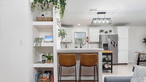 A modern kitchen with white cabinetry, a stainless steel refrigerator, and two brown bar stools. - Bright 4BR Home - Just Minutes from town & Beach! (St. Augustine)