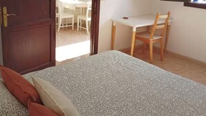 Ein Schlafzimmer mit Bett, Schreibtisch und Stuhl. Eine Tür führt in einen anderen Raum.