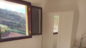 Ένα μικρό δωμάτιο με ένα λευκό τραπέζι και μια καρέκλα, μια ντουλάπα και ένα γραφείο με ένα φωτιστικό.