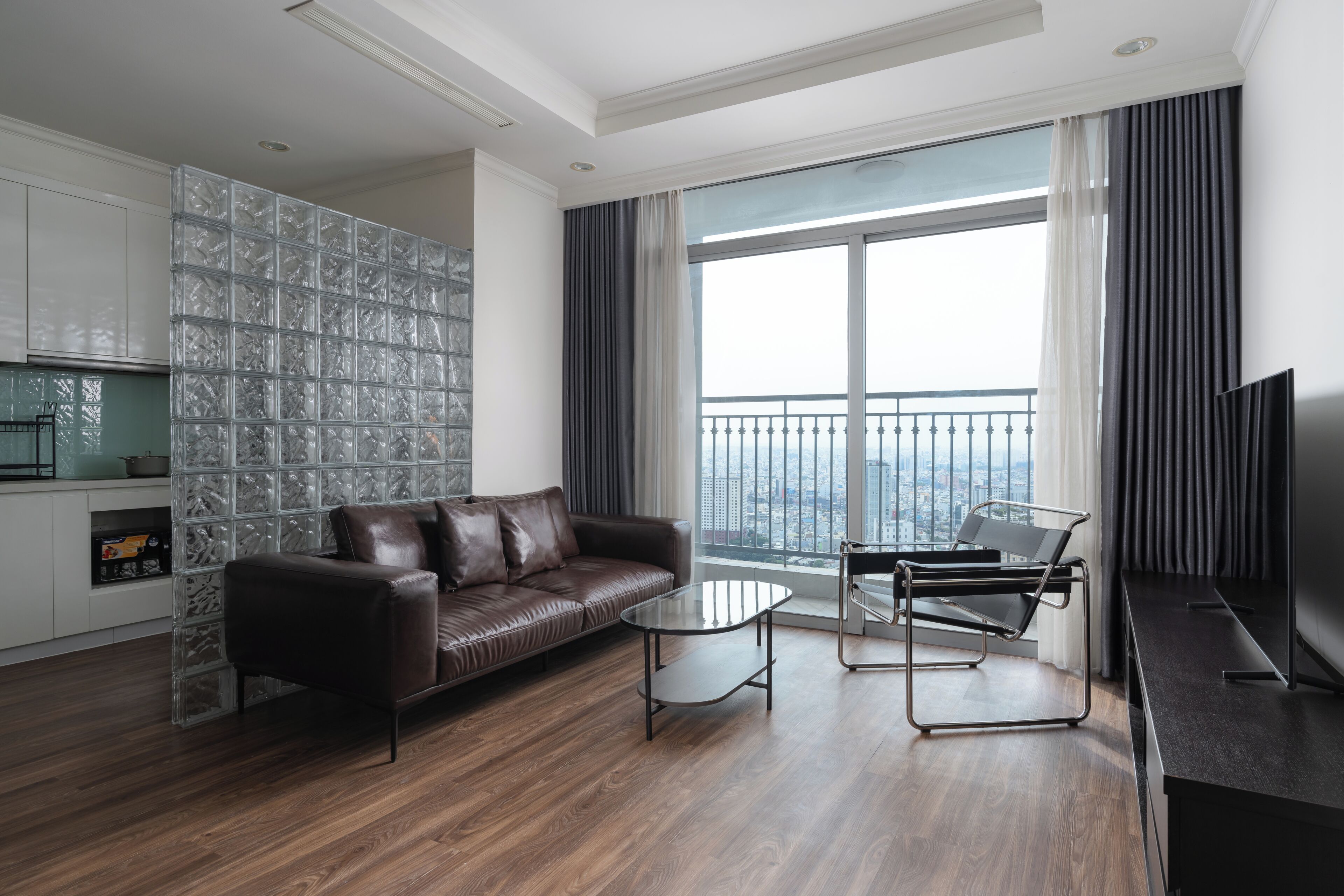 A modern living room with a leather sofa, a glass coffee table, a metal chair, and a TV.