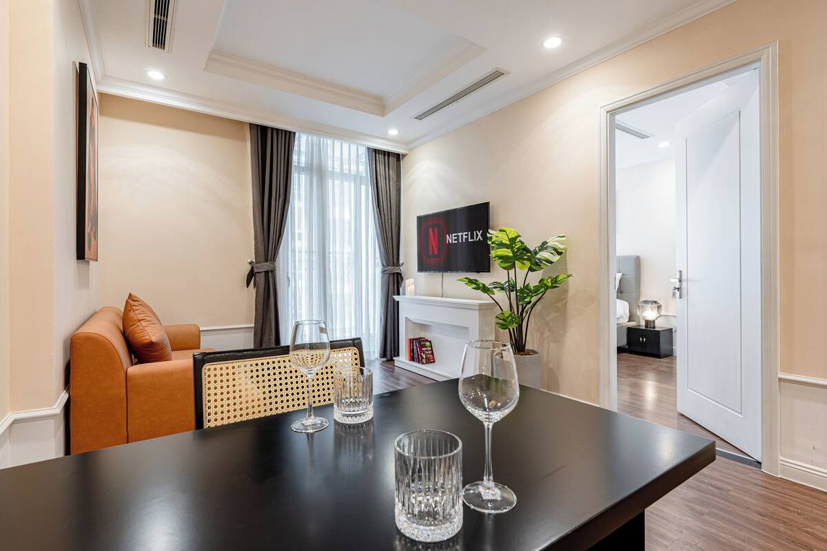 Una sala de estar moderna con un sofá, una mesa de centro con copas de vino, una chimenea y un televisor que muestra el logotipo de Netflix.