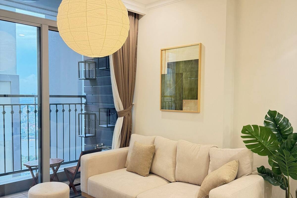 Una sala de estar moderna con un sofá beige, una mesa de centro de madera, una lámpara colgante grande y una planta en maceta.