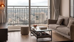 Una sala de estar moderna con un sofá, una mesa de centro y vistas de la ciudad a través de amplios ventanales.