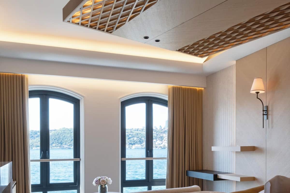 Ein modernes Hotelzimmer mit einem großen Bett, einem Schreibtisch und Meerblick durch große Fenster.