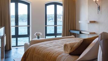 Une chambre d’hôtel moderne, dotée d’un grand lit, d’un bureau et offrant une vue sur la mer grâce à de larges fenêtres.