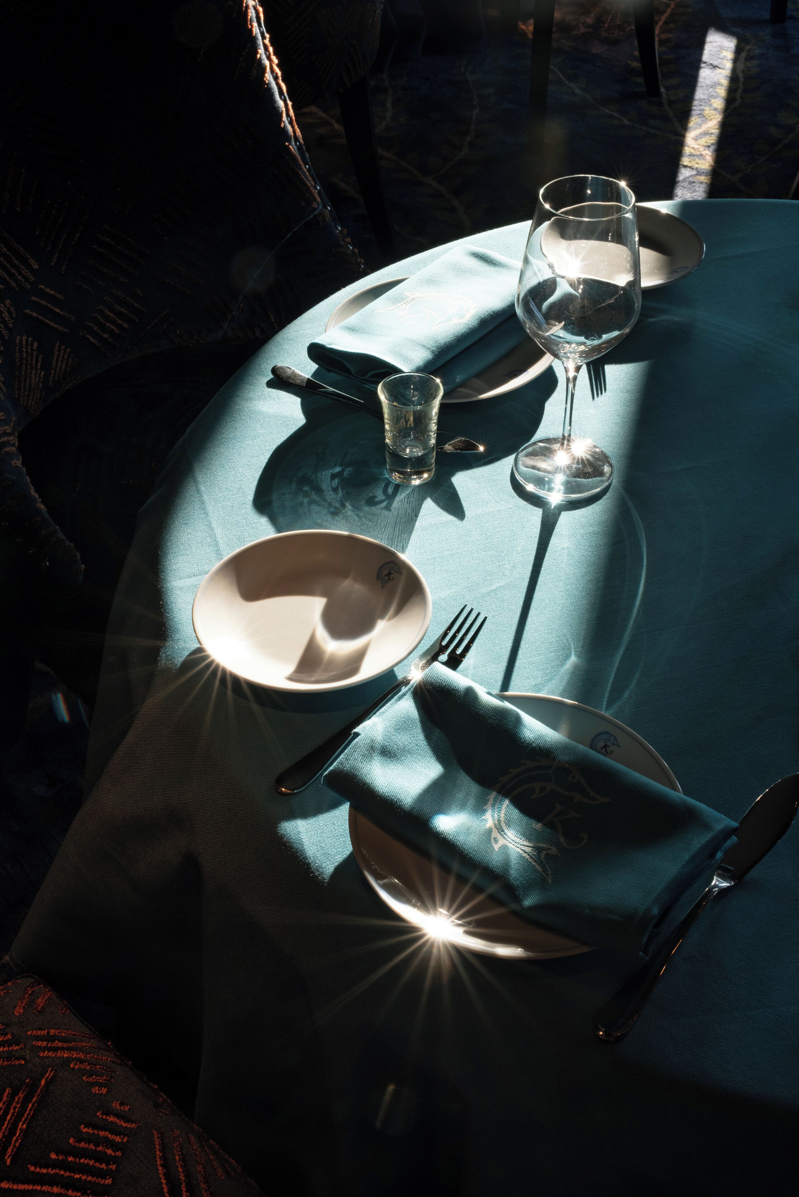 Uma mesa posta com um copo de água, uma taça de vinho, um prato, um garfo e uma guardanapo.