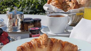 A croissant on a plate, a cup of coffee, and a glass of orange juice on a table with a view of a boat in the background.
