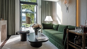 Ein modernes Hotelzimmer mit einem grünen Sofa, einem Couchtisch mit Blumenvase, einer Lampe und Blick ins Freie.