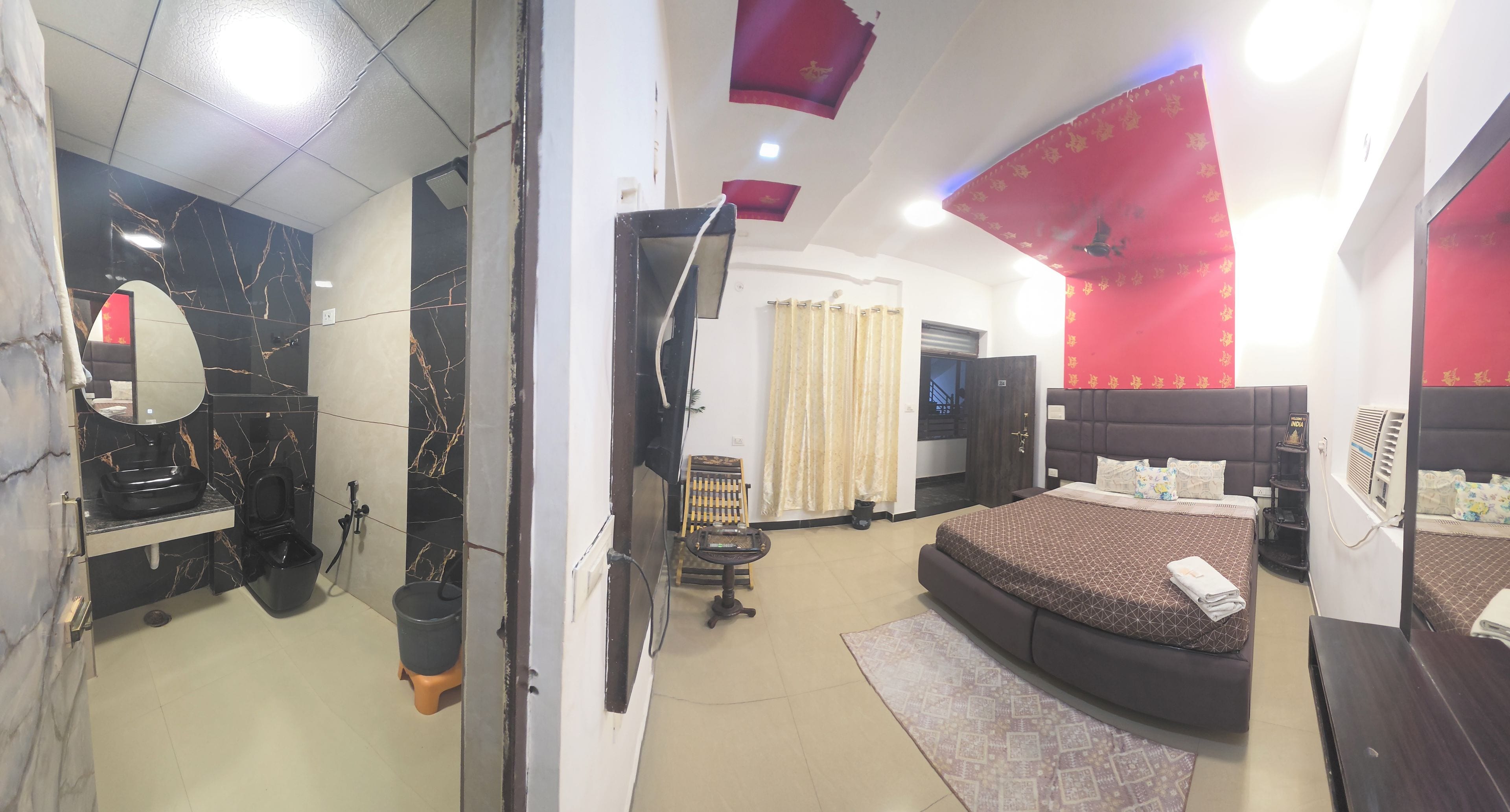 A bedroom with a bed, a TV, a mirror, and a bathroom with a sink and toilet.