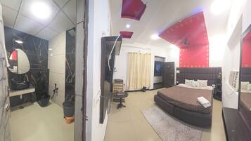 A bedroom with a bed, a TV, a mirror, and a bathroom with a sink and toilet.