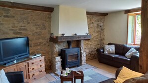 A living room with a stone wall, a fireplace, a television, a sofa, and a window.